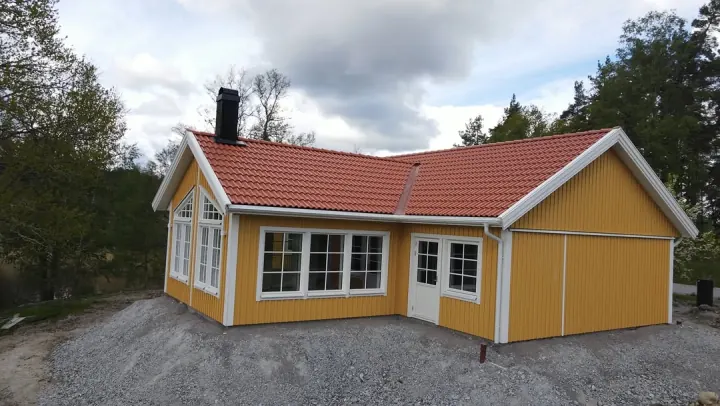Nybyggt gult fritidshus med tegelrött tak — Premie Bygg